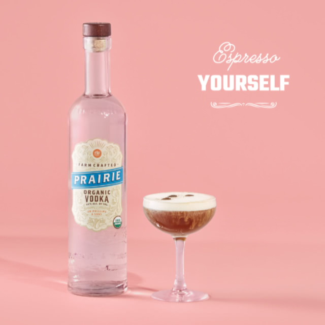 An espresso martini next to a bottle of Prairie vodka on a pink background